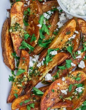 Greek oven fries garnished with parsley and feta with a side of Tzatziki sauce