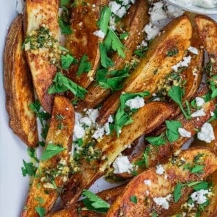 Greek oven fries garnished with parsley and feta with a side of Tzatziki sauce