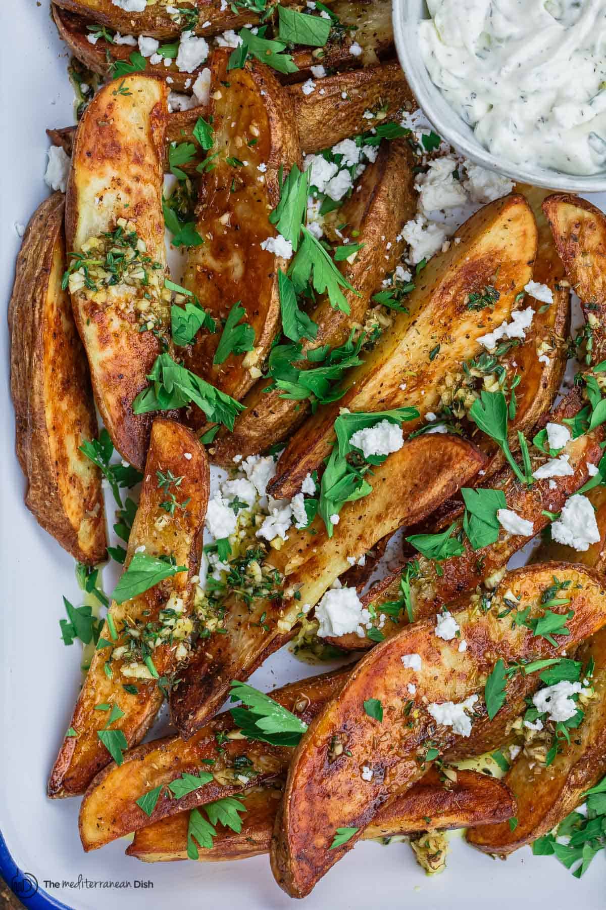 Greek oven fries garnished with parsley and feta with a side of Tzatziki sauce