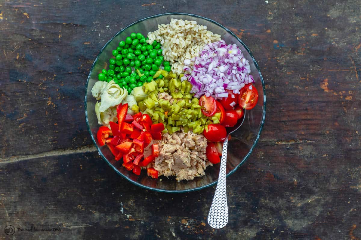 rice, tuna, onions, cherry tomatoes, bell peppers, and artichoke hearts in a bowl to make rice salad