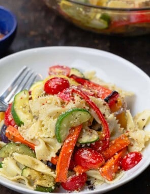 Pasta primavera with roasted veggies in a bowl. A large serving bowl to the side
