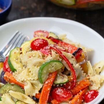 Pasta primavera with roasted veggies in a bowl. A large serving bowl to the side