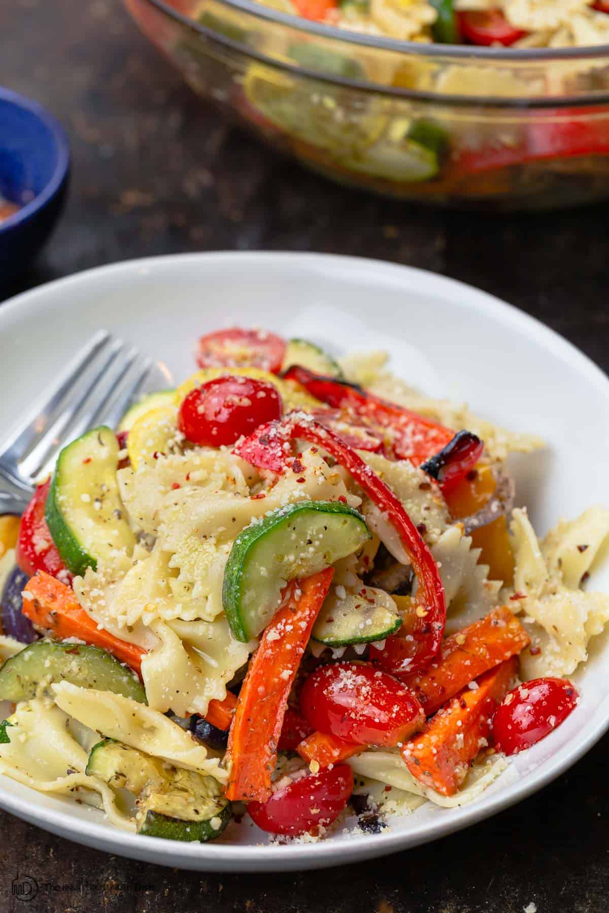 Pasta primavera with roasted veggies in a bowl. A large serving bowl to the side