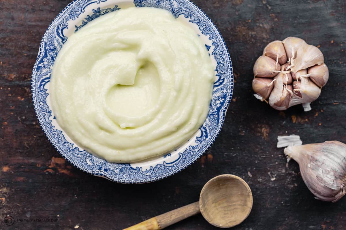 A blue bowl of toum garlic sauce and a spoon to serve