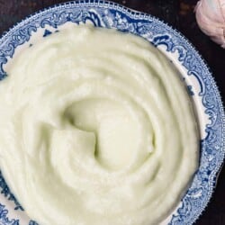 toum garlic sauce in a blue bowl. garlic head to the side