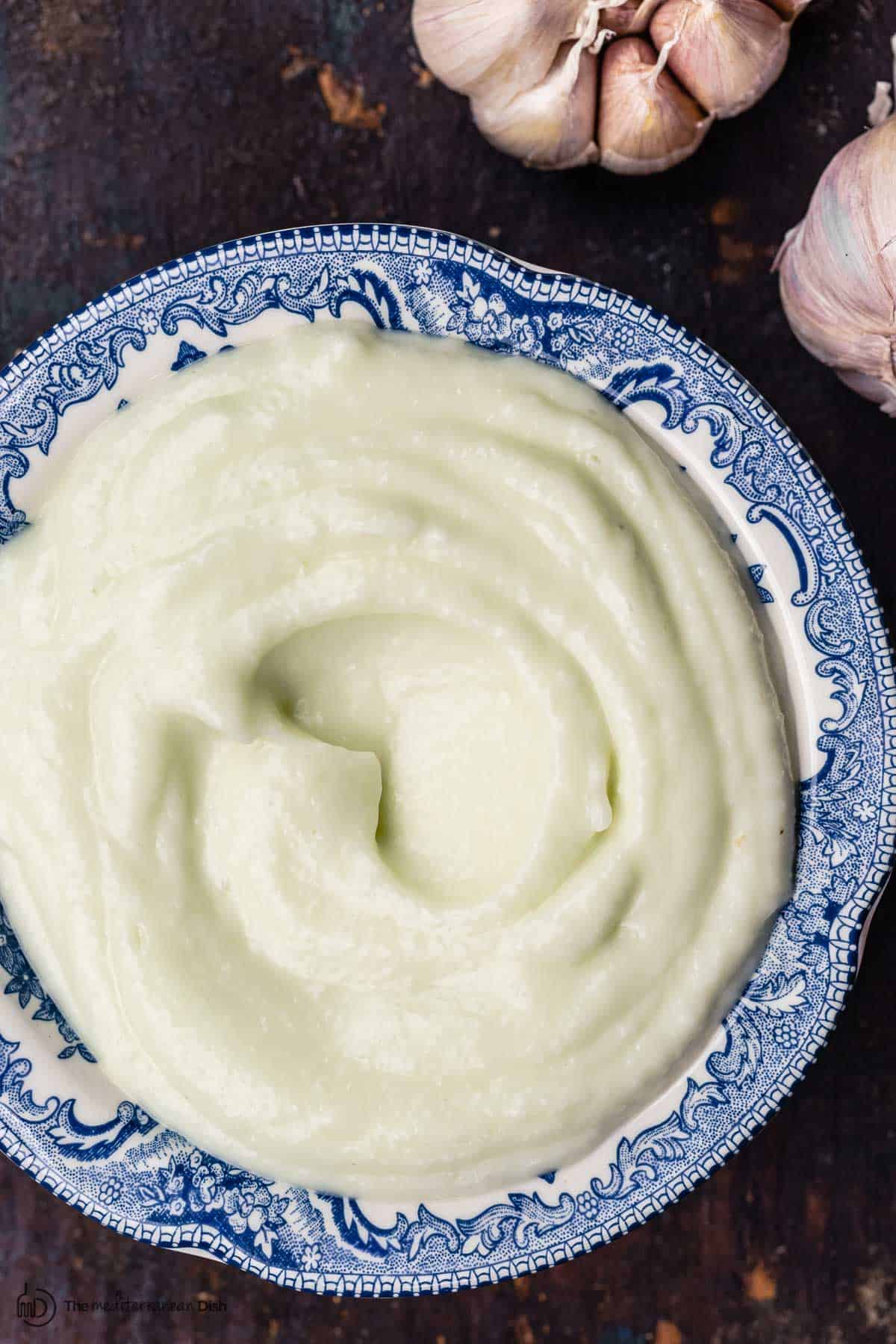 toum garlic sauce in a blue bowl. garlic head to the side