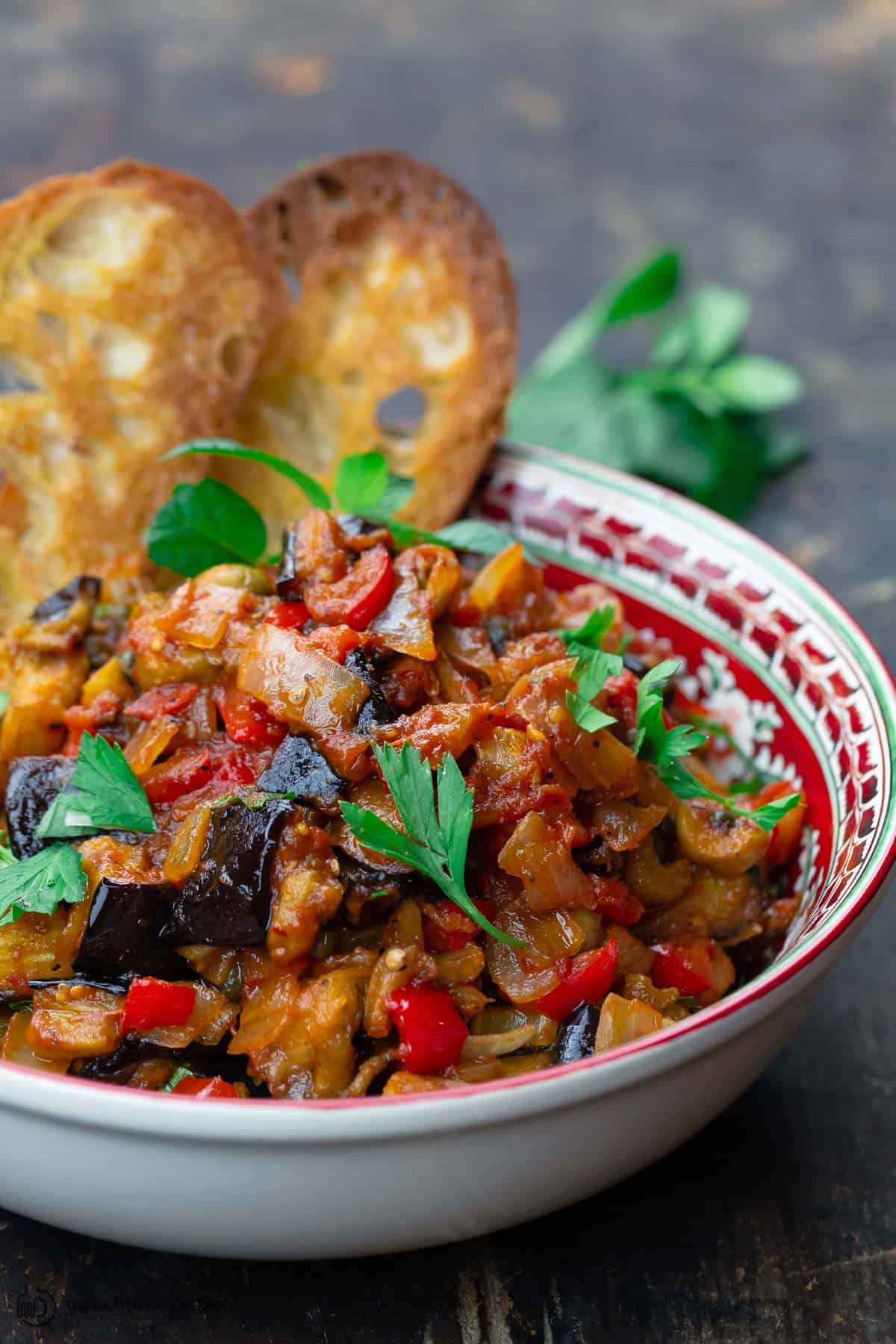 eggplant caponata served in a bowl with toasted ciabatta bread