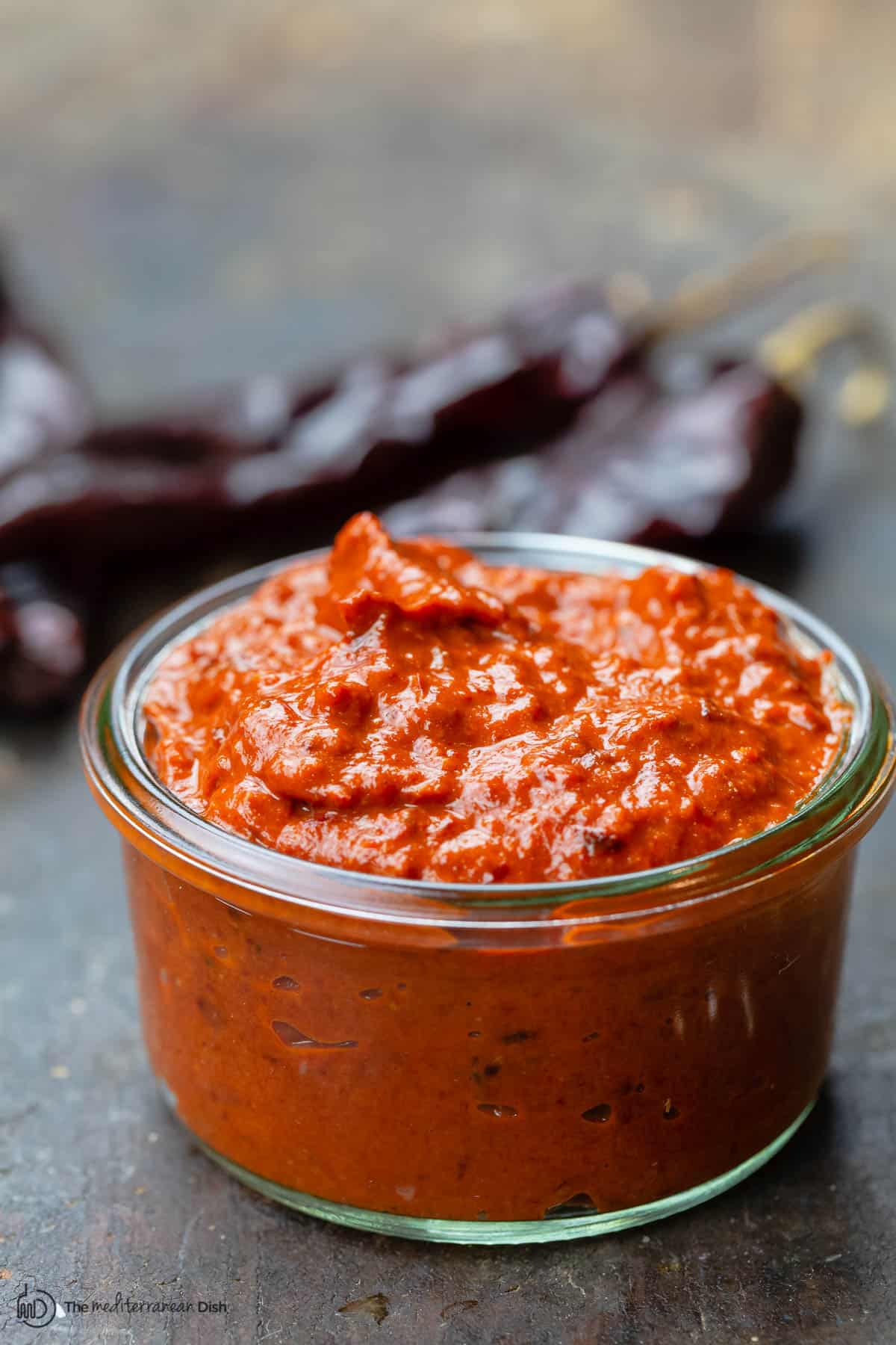 homemade harissa in a small open jar. Dry chiles to the side