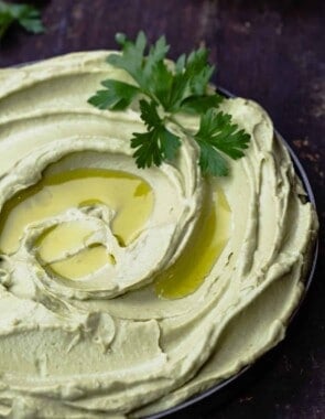 avocado hummus in a bowl with a little extra virign olive oil and a garnish of parsley