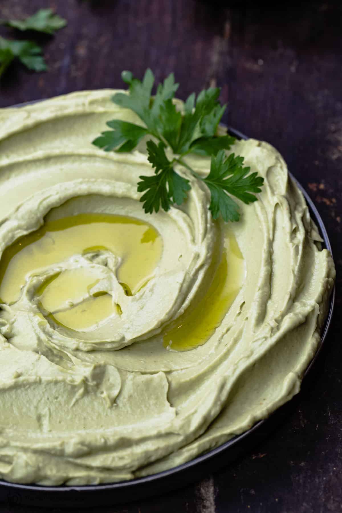 avocado hummus in a bowl with a little extra virign olive oil and a garnish of parsley