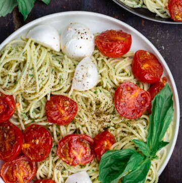 pesto pasta on two plates with a side of fresh basil