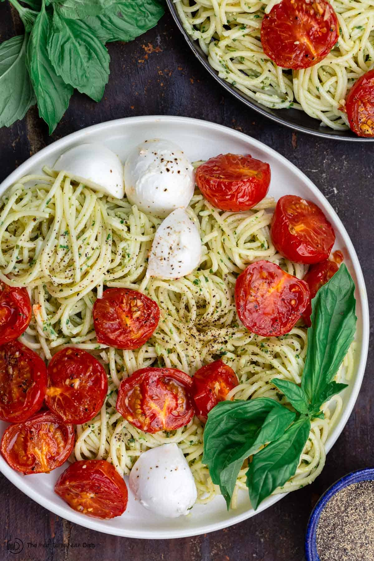 pesto pasta on two plates with a side of fresh basil