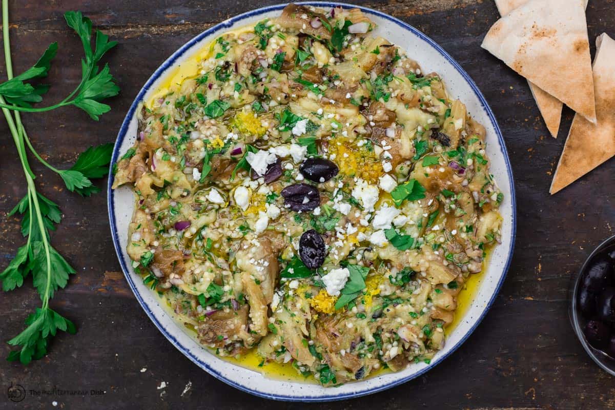 eggplant dip in a serving dish with a side of pita and olives