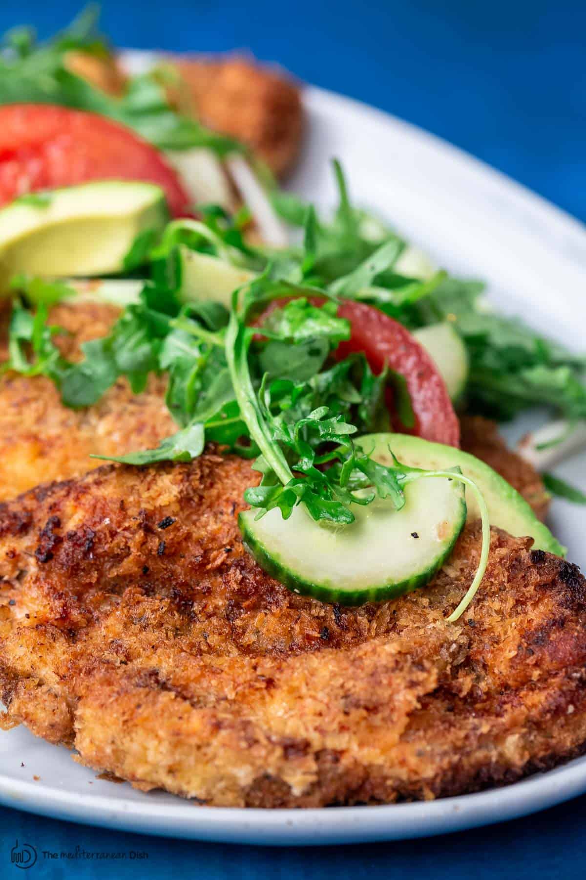 chicken schnitzel on a platter with arugula salad