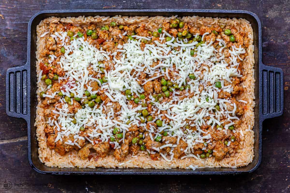 Layers of rice, sausage and peas in a baking dish