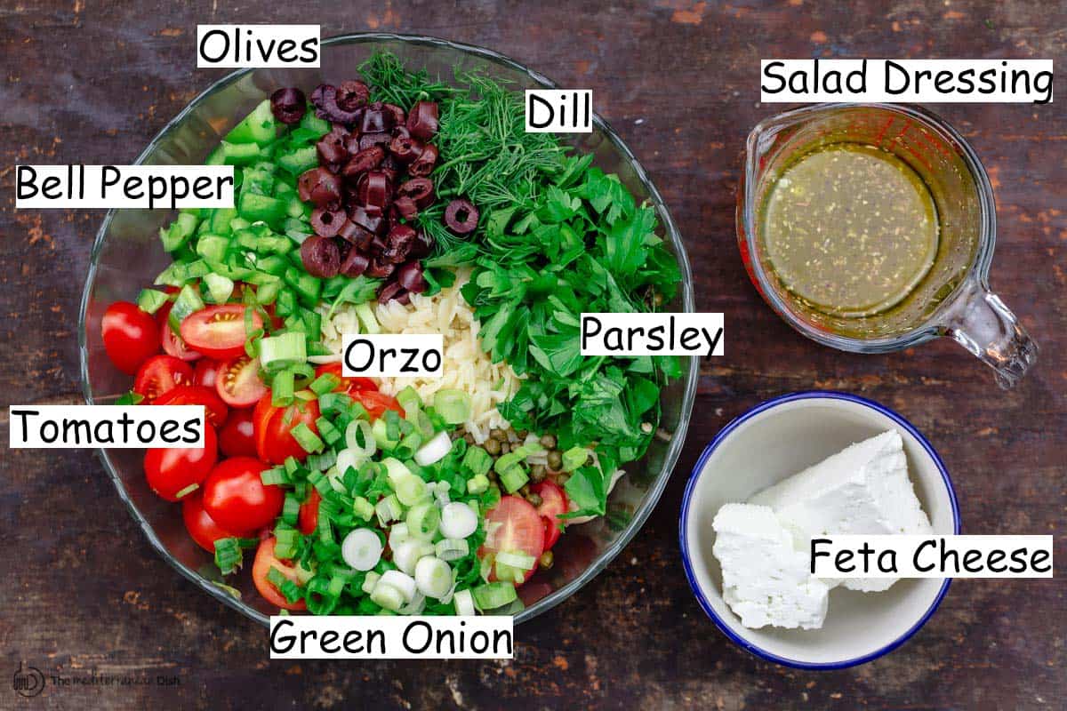 ingredients for orzo salad including olives, bell pepper, tomatoes, green onion, orzo, parsley, dill, salad dressing, and feta cheese.