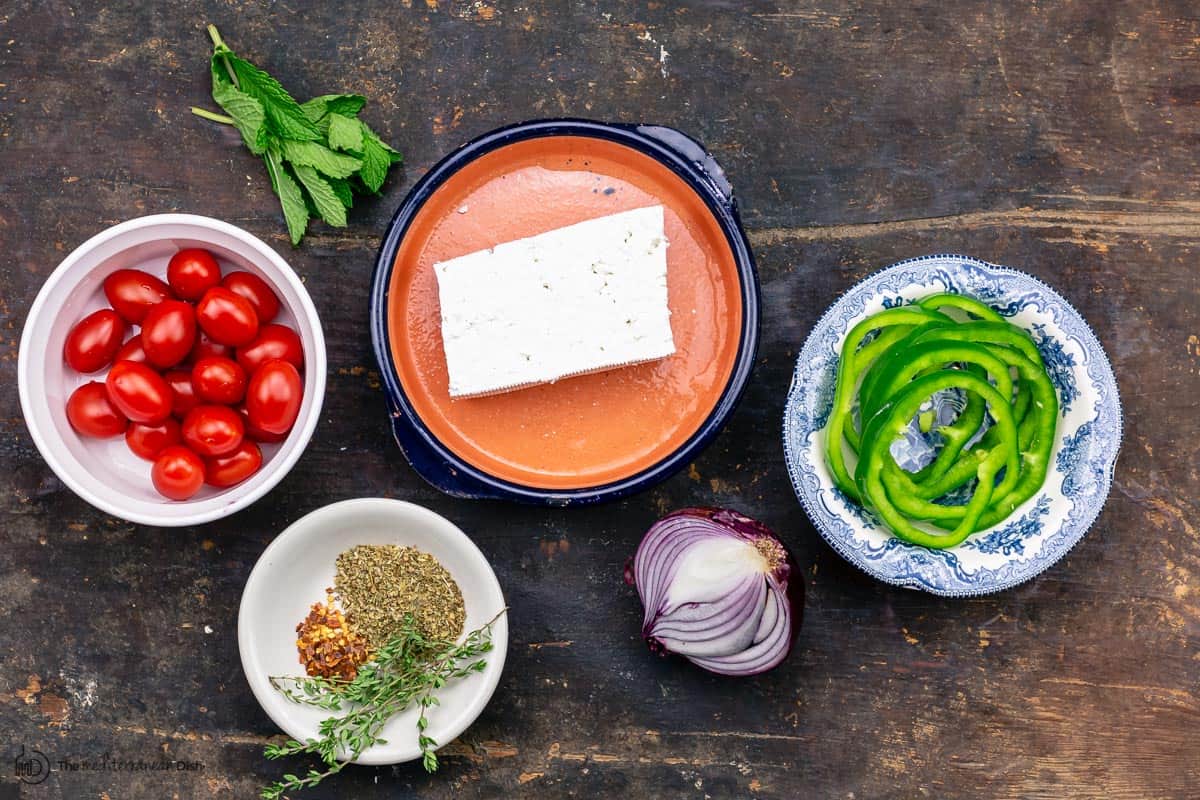 ingredients for baked feta: tomatoes, peppers, red onions, herbs, and block of feta