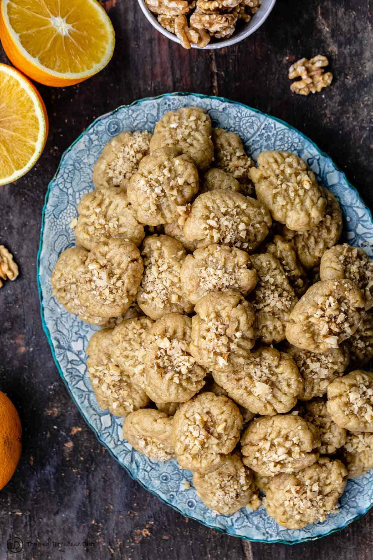 Melomakarona cookies ona platter with walnuts and an orange to the side