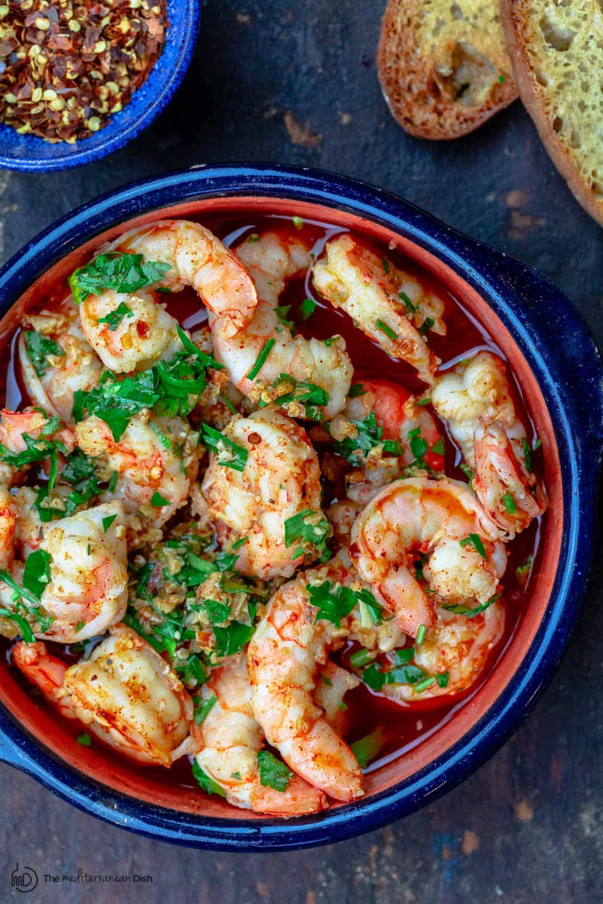 Spanish garlic shrimp with a side of bread and hot red pepper flakes