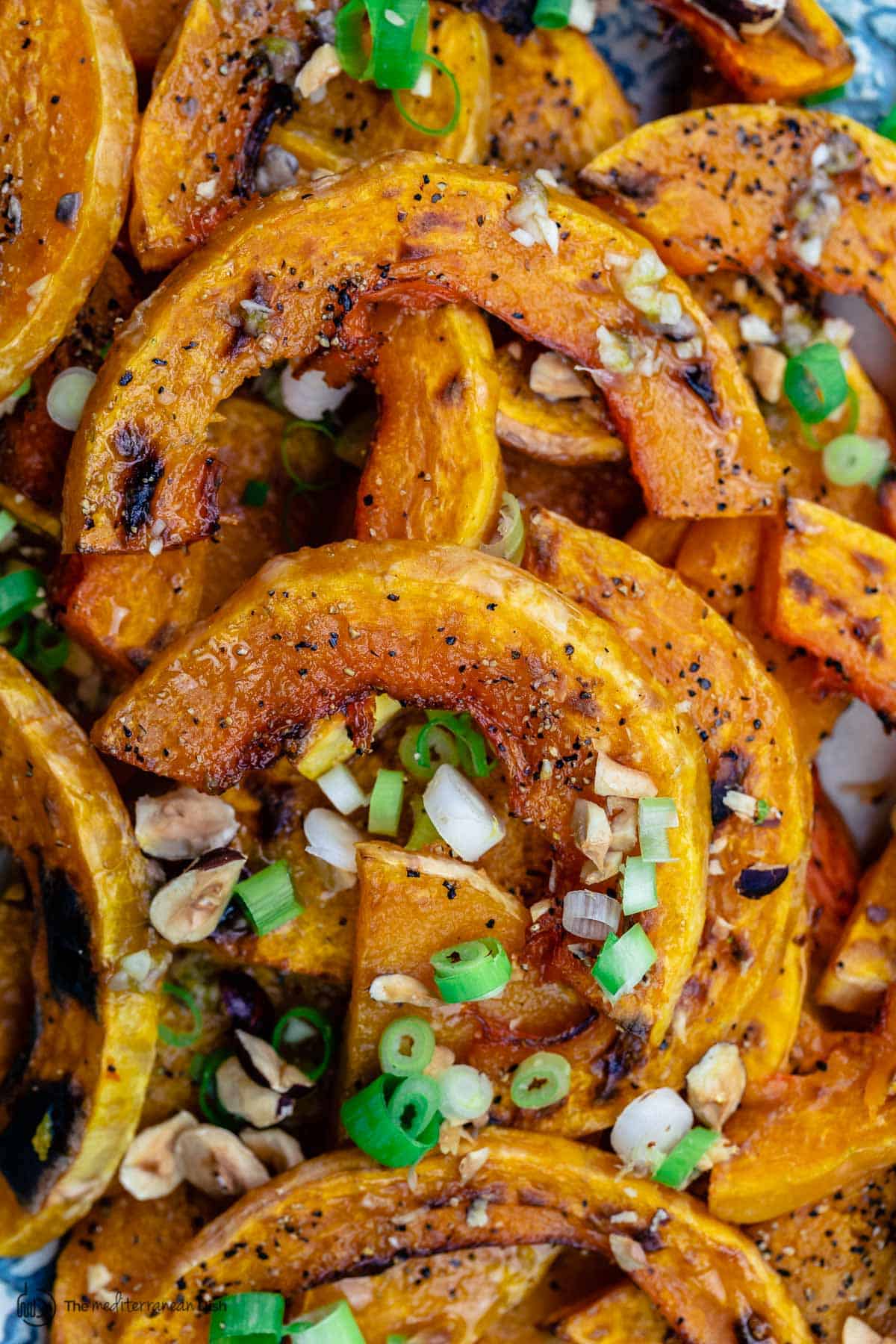 closeup of butternut squash slices with nuts and scallions