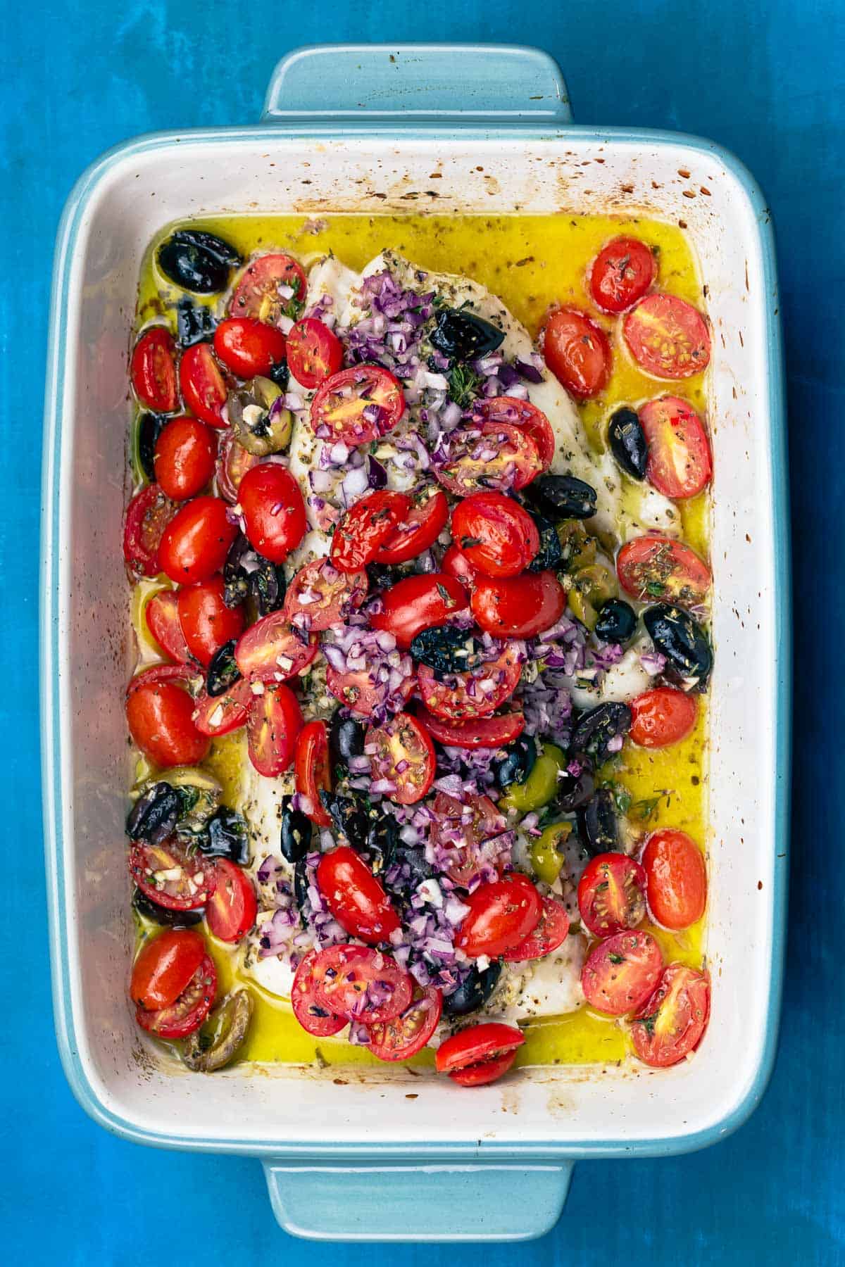 baked white fish in a baking dish, topped with tomatoes, olives and onions