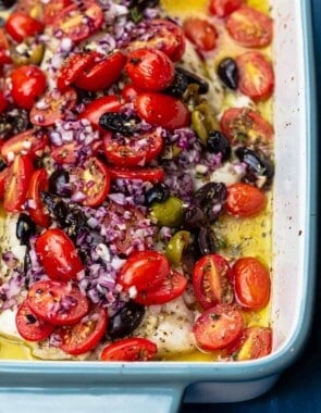 Mediterranean baked white fish in a backing dish adn covered with fresh tomatoes, olive oil, onion and olives.