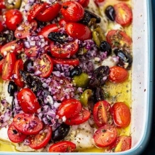 Mediterranean baked white fish in a backing dish adn covered with fresh tomatoes, olive oil, onion and olives.