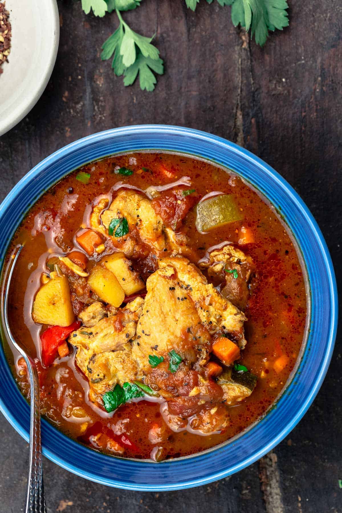 chicken stew served in a bowl with a side of crushed red pepper flakes