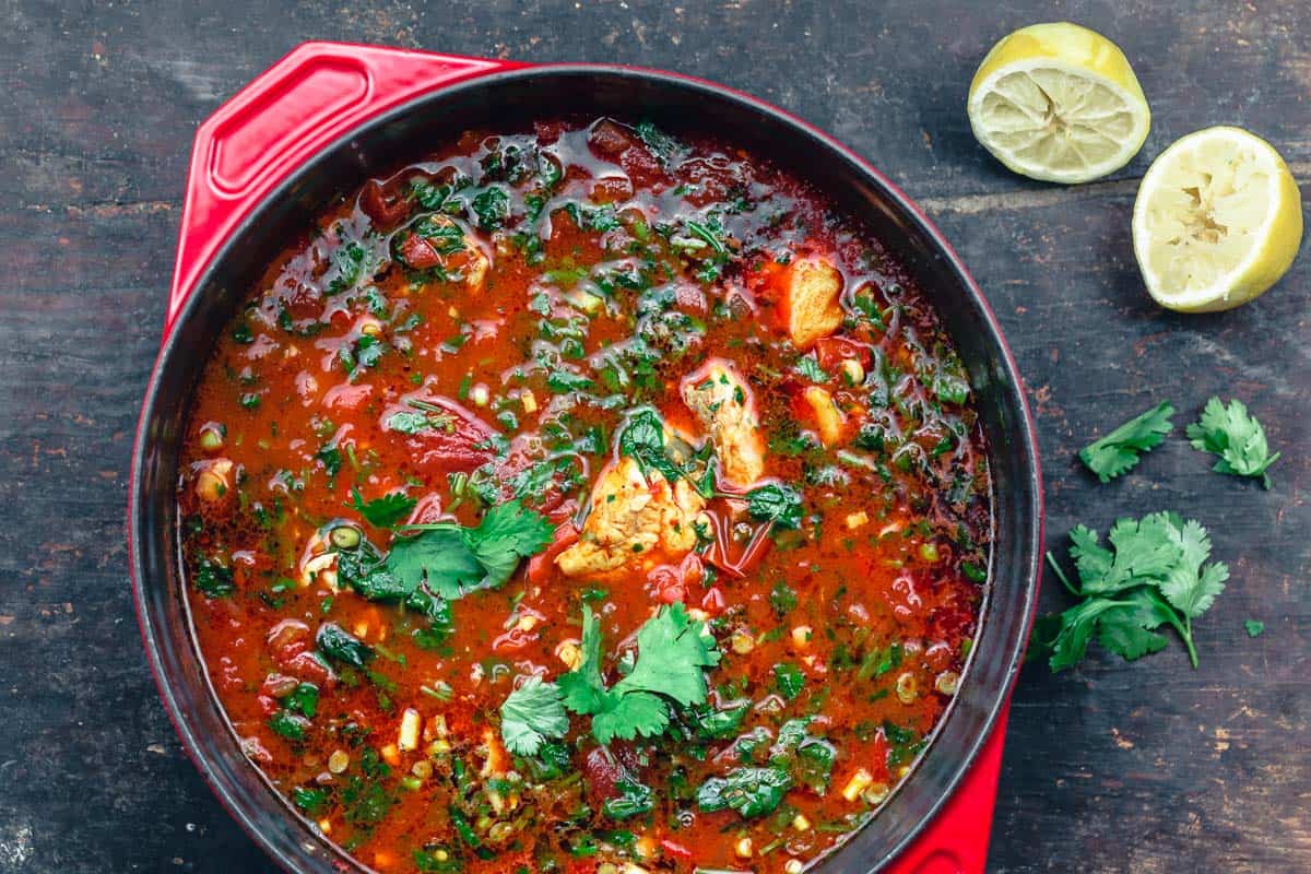 fish soup garnished with parsley and cilantro with a side of cut lemons