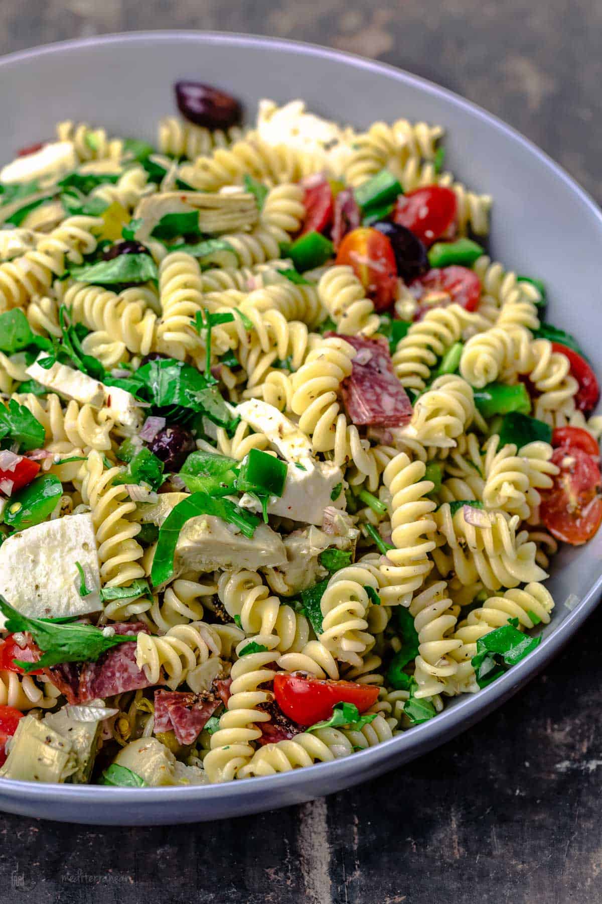 Italian pasta salad with fresh veggies, mozzarella and salami, tossed in a big bowl 