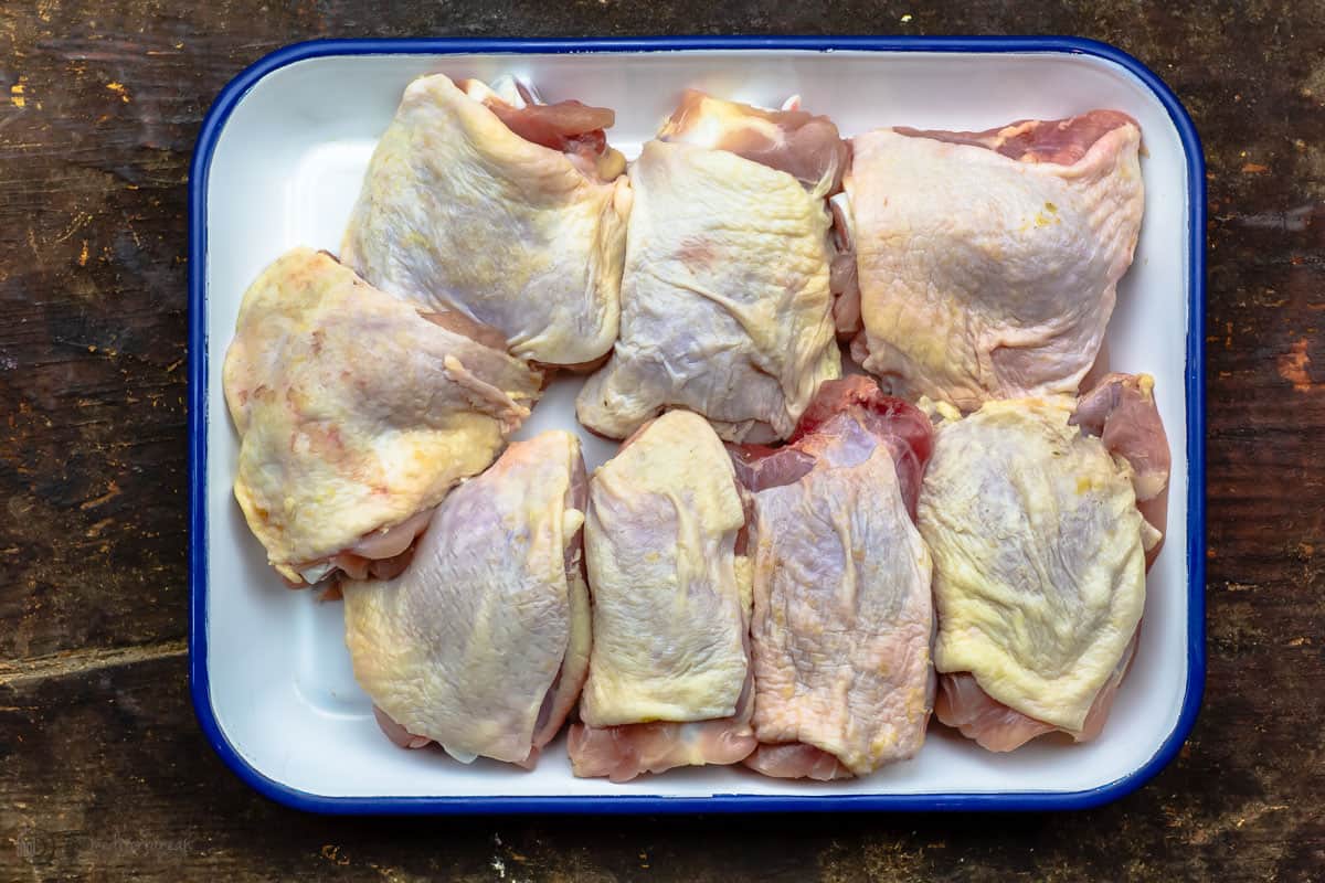 Raw chicken thighs with skin on place on a baking pan