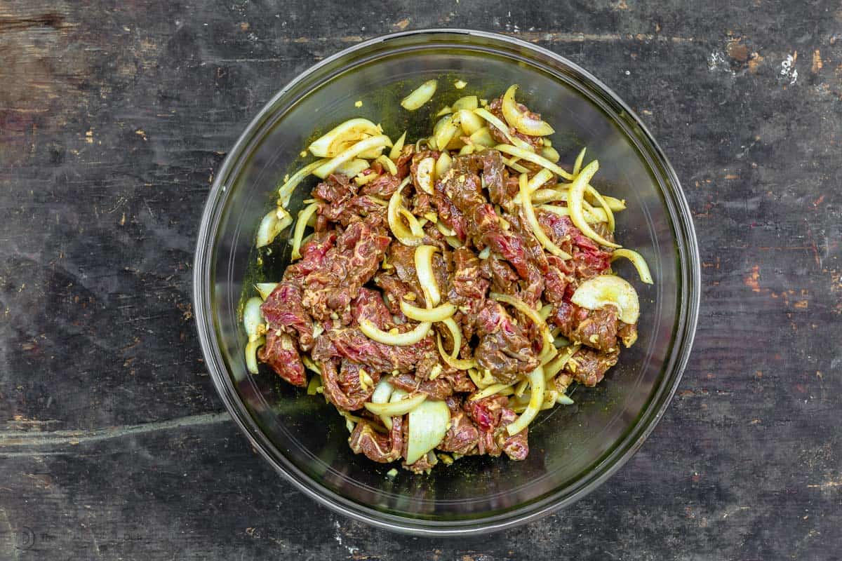 Sliced beef marinating in a bowl with spices and onions