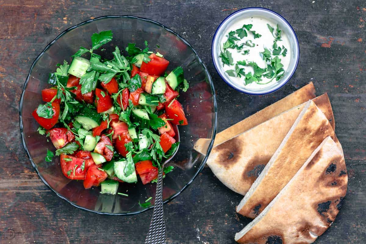 Salad mixed in bowl with a side of tahini and pita bread