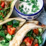 Beef shawarma pitas served on a blue plate with a side of tahini sauce