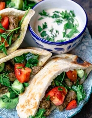 Beef shawarma pitas served on a blue plate with a side of tahini sauce