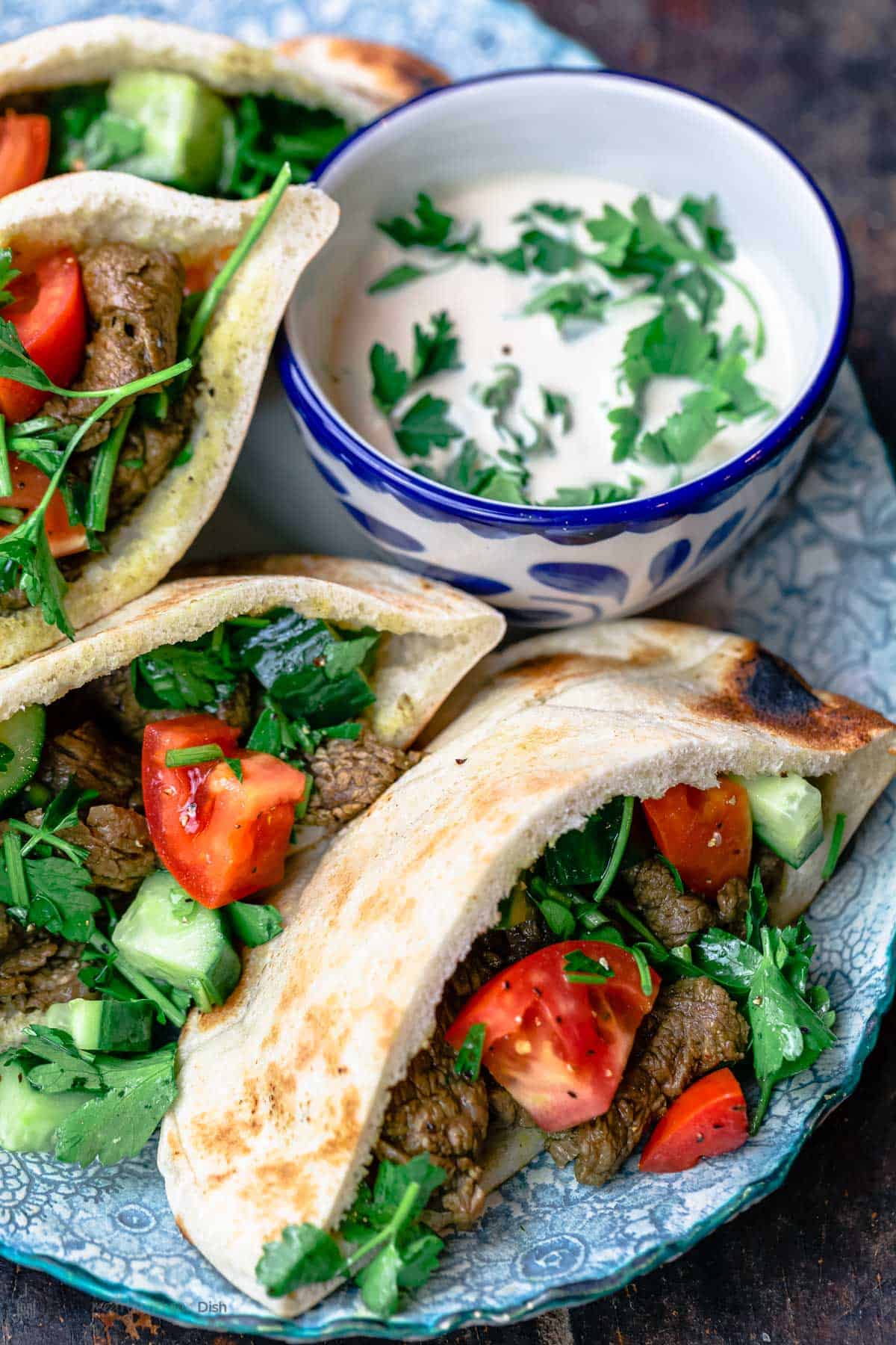 Beef shawarma pitas served on a blue plate with a side of tahini sauce