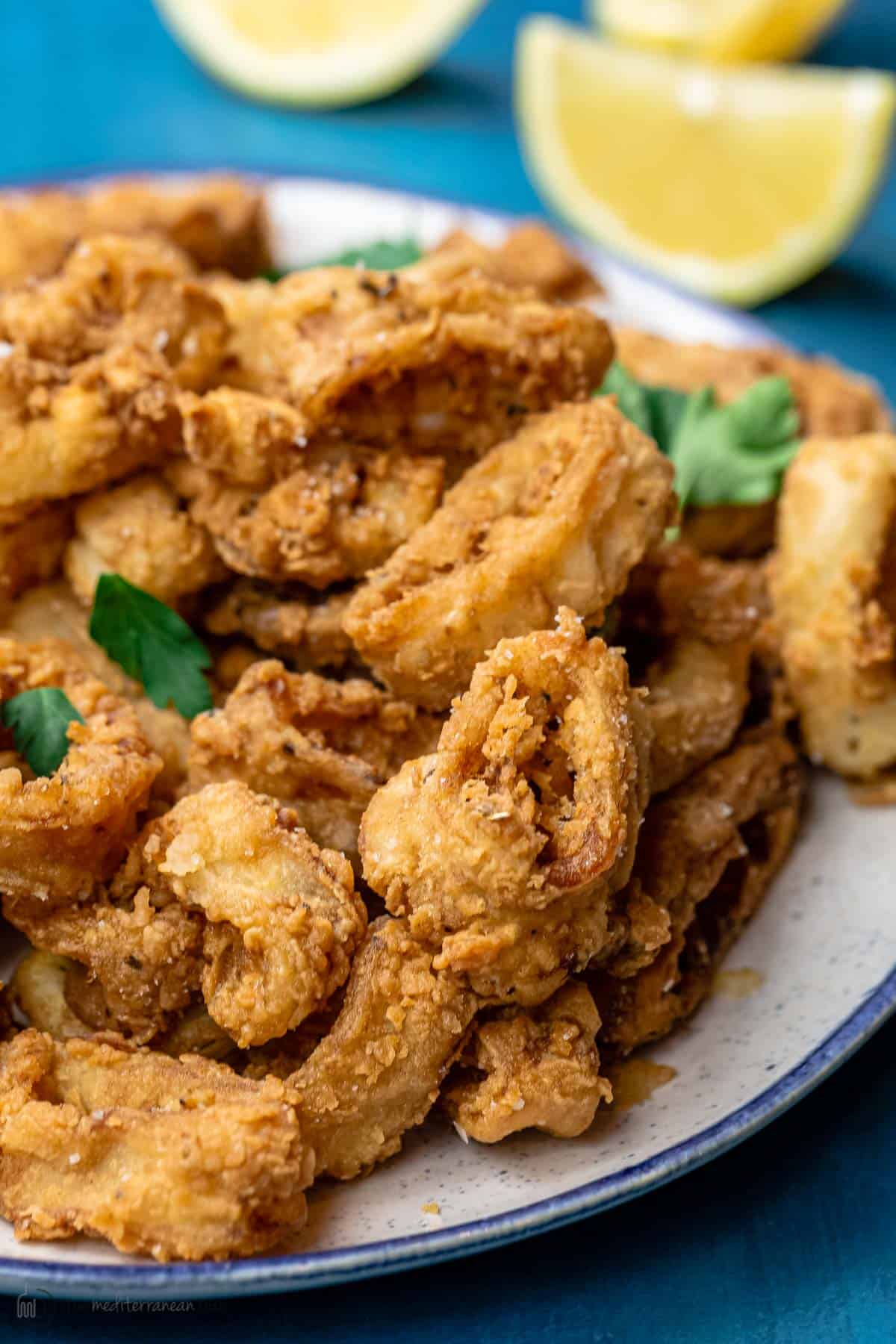 Fried calamari served on a plate with some lemons in the background