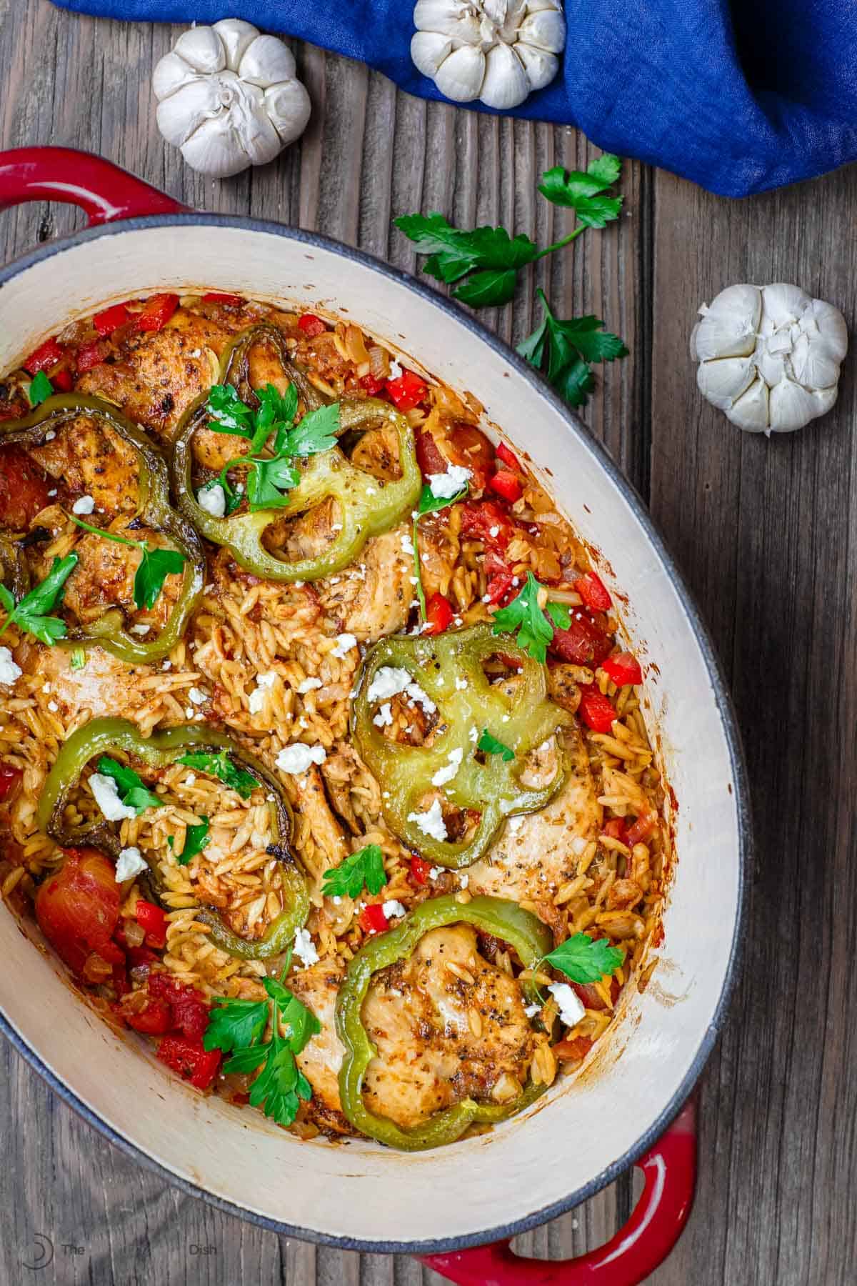 Chicken and orzo dinner served in a large pot with heads of garlic on table