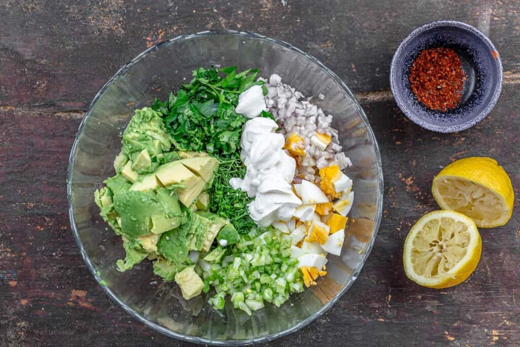 ingredients for egg salad in a bowl. lemons and pepper flakes to the side