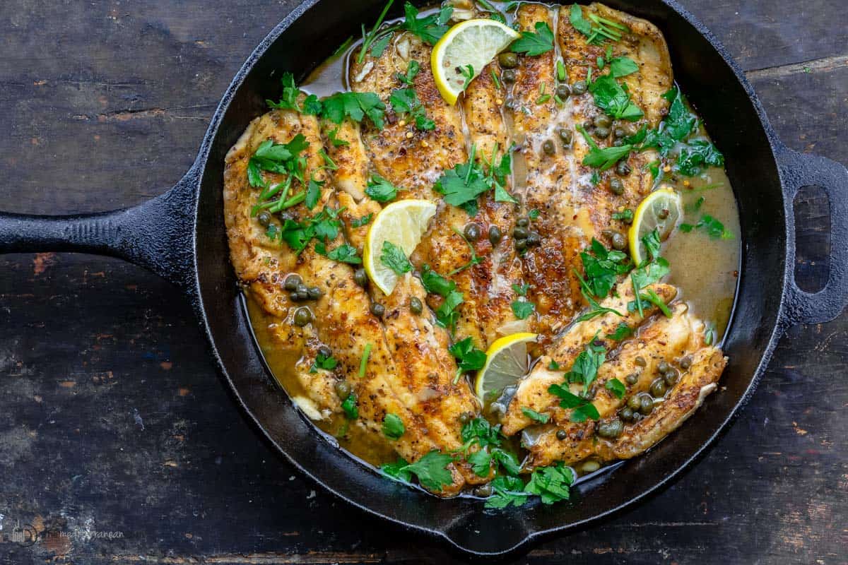 Fish piccata topped with lemon slices and parsley in a skillet