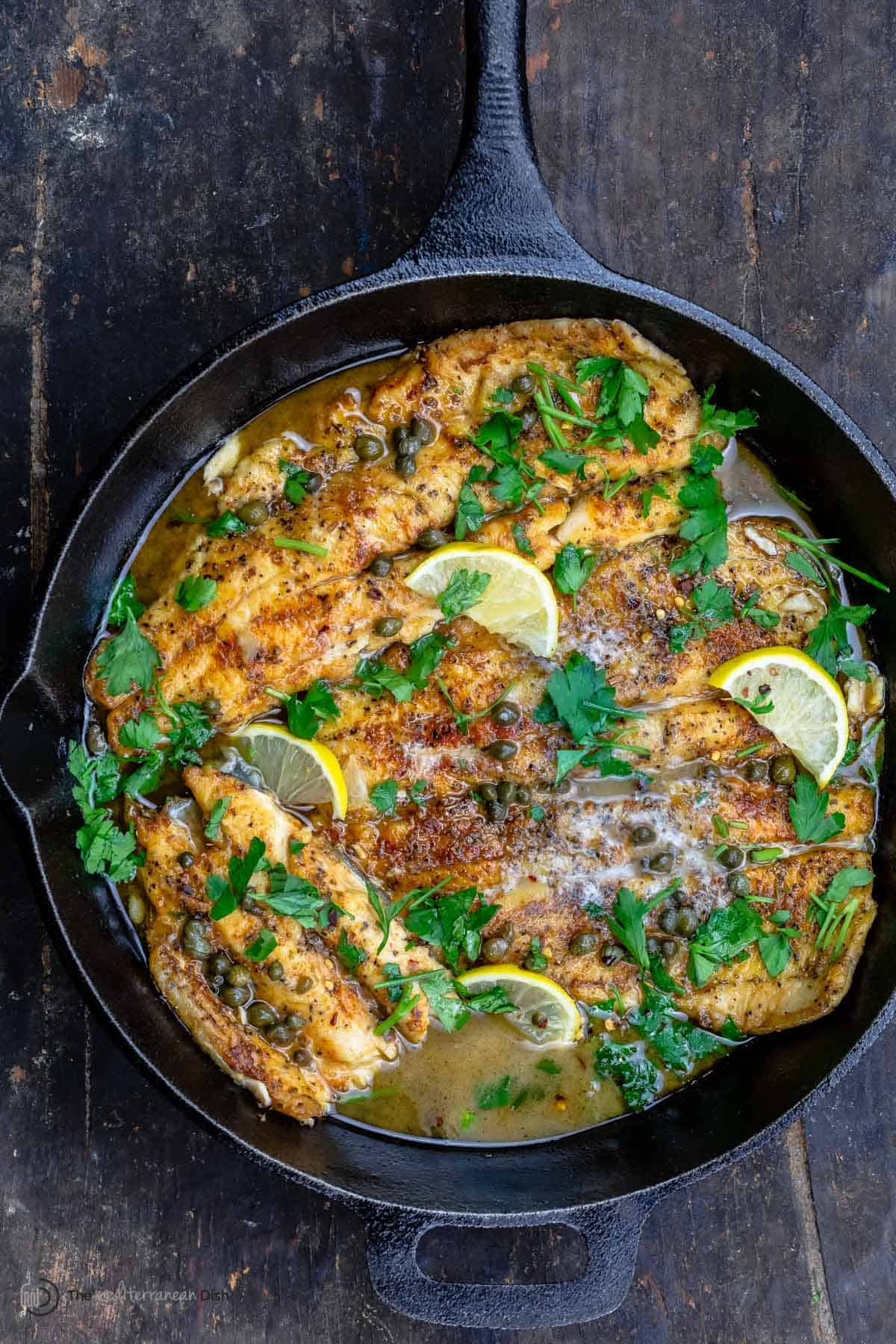 Pan-seared trout topped with a lemon piccata sauce in a cast iron skillet