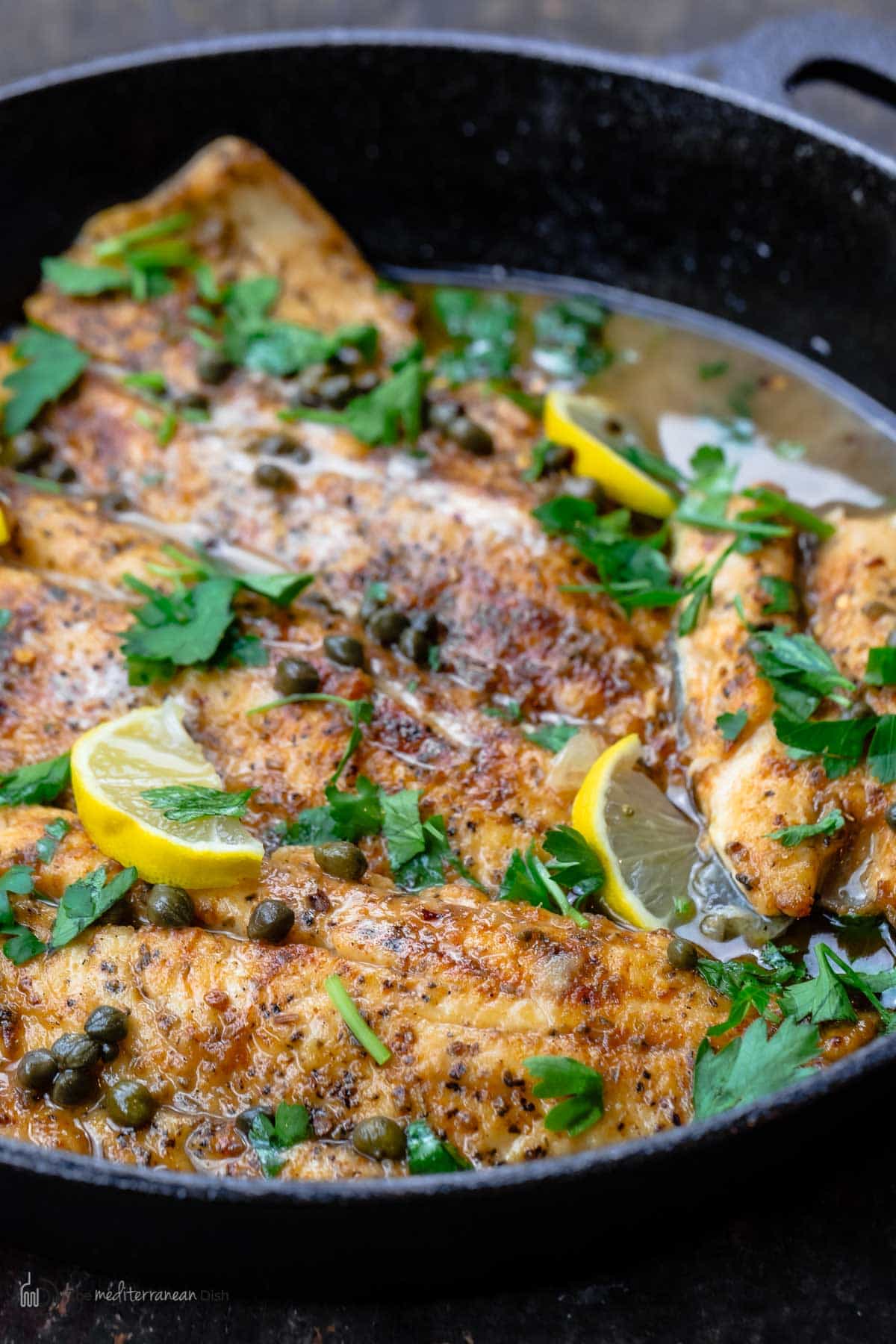 A skillet of fish piccata topped with parsley