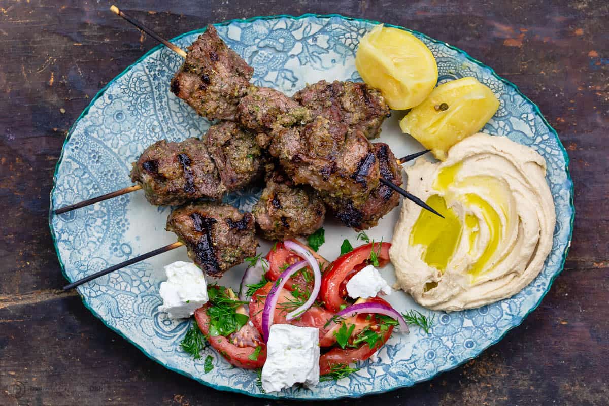 Lamb kabobs served on a plate with a salad and hummus