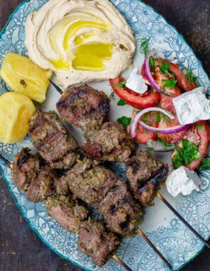 Lamb kabobs served on a plate with a tomato salad and hummus