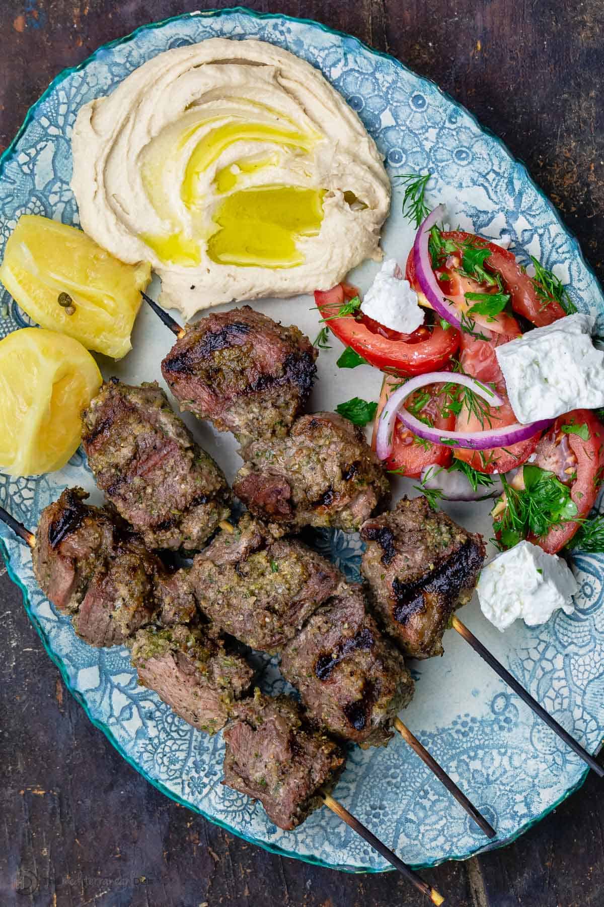 Lamb kabobs served on a plate with a tomato salad and hummus