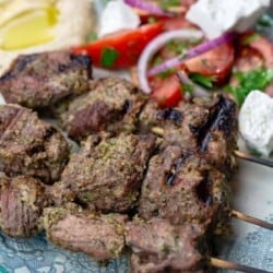Lamb kabobs served on a plate with a tomato salad and hummus