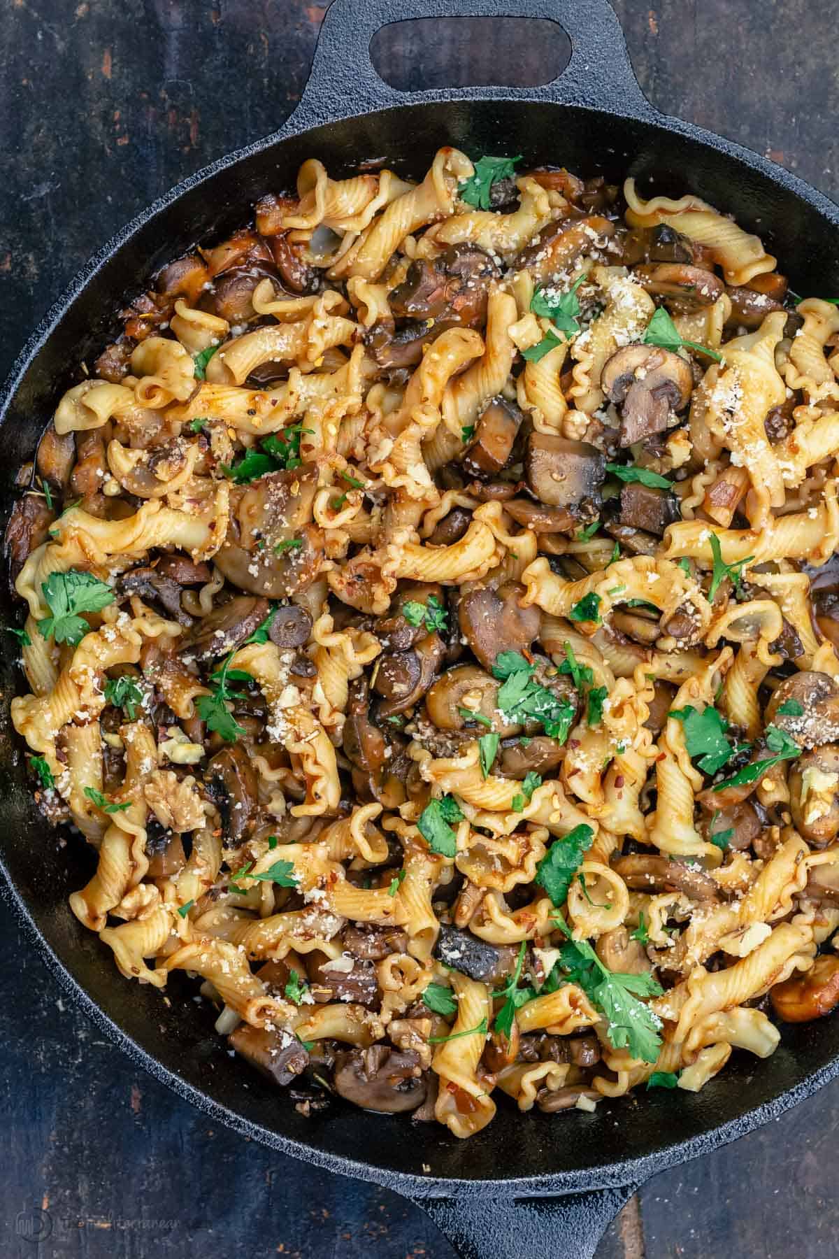 A skillet with pasta and mushrooms, finished with parsley