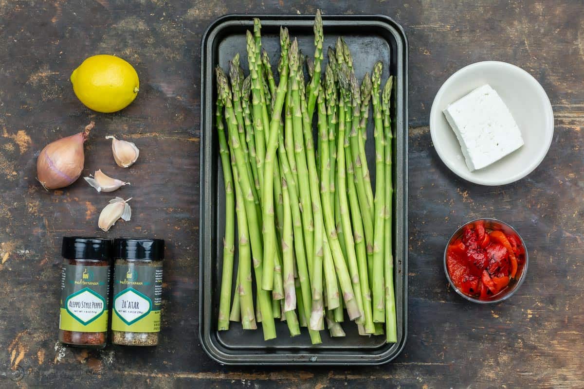 the ingredients for Mediterranean sauteed asparagus - a lemon, garlic cloves, spices, asparagus, roasted red peppers and feta.