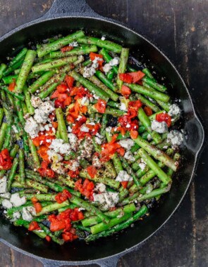 Sauteed asparagus topped with feta and roasted red peppers in a cast iron skillet