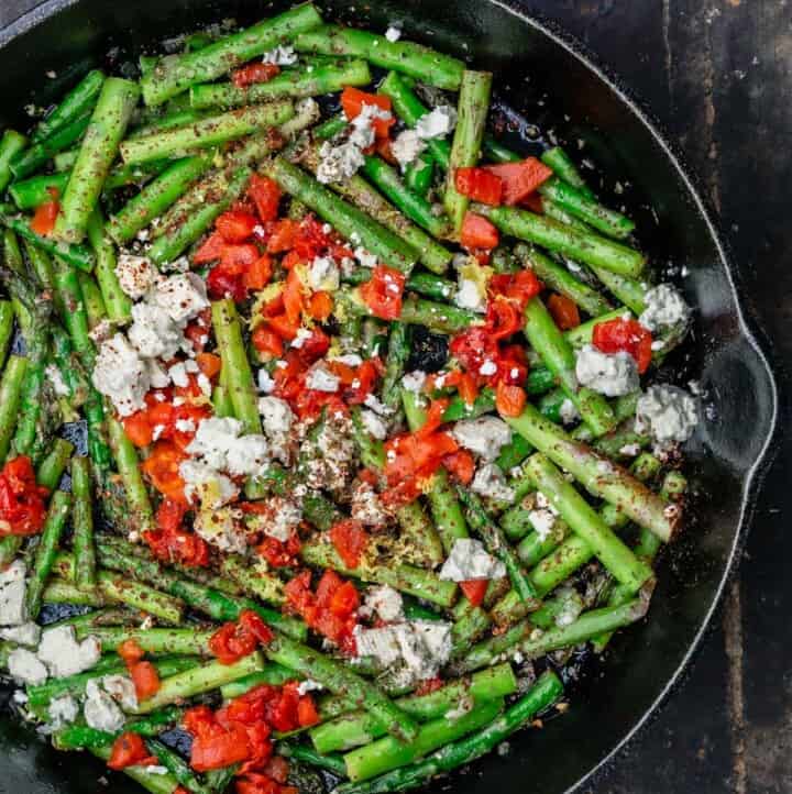 Sauteed asparagus topped with feta and roasted red peppers in a cast iron skillet
